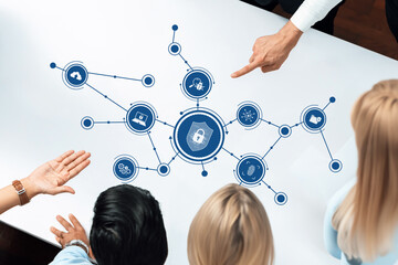 A diverse group of professionals collaborates around a table, analyzing an innovative security technology concept represented by various digital protection icons and connections. Amity