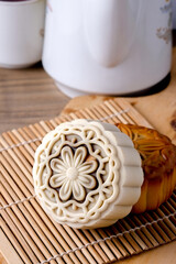  A close-up shot of two mooncakes on a bamboo mat, with a white teapot and a teacup blurred in the background.