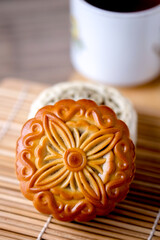 Traditional mooncake with intricate floral pattern placed on bamboo mat, symbolizing Mid Autumn Festival celebration and Asian pastry culture.