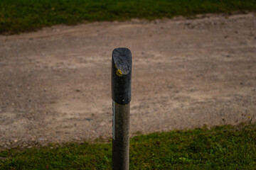 A solitary concrete road marker with a black rounded top and moss, placed beside a dirt path and...