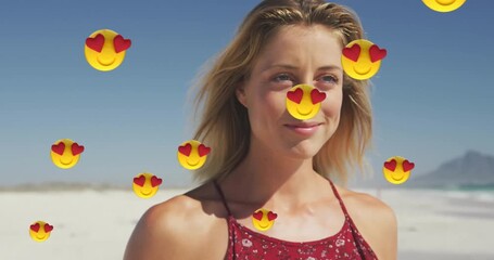 Animation of emojis over smiling beautiful caucasian woman walking at beach against sky - Powered by Adobe