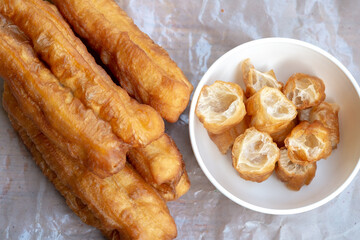 A close-up, top-down view of Youtiao, also known as Chinese fried dough sticks or Cakwe in Southeast Asia, with some pieces cut up and served in a white bowl. These crispy, airy golden-brown delights 