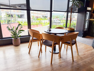 Round dining table with chairs near large window overlooking outdoor view. Hospitality, leisure, and social atmosphere for guests enjoying restaurant setting.