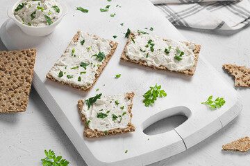Crispbread toast with Cottage Cheese and parsley on white wooden board.