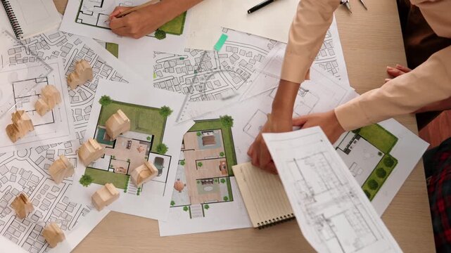 Architect and safety engineer discussion about building construction use blueprint on table with architectural document, measurement tool and wooden block scatter around at modern office. Delineation.
