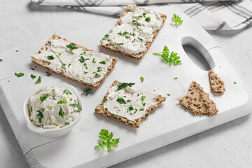 Crispbread toast with Cottage Cheese and parsley on white wooden board.