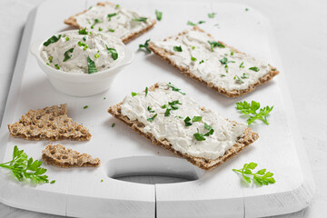 Crispbread toast with Cottage Cheese and parsley on white wooden board.