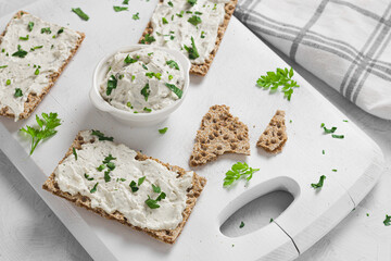 Crispbread toast with Cottage Cheese and parsley on white wooden board.