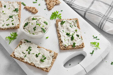 Crispbread toast with Cottage Cheese and parsley on white wooden board.