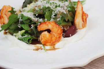Salad of leaves, shrimp, cheese and avocado in a plate on a wooden table