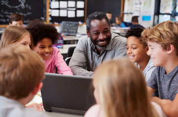 Diverse group of children with male teacher using latop together in modern schol classroom