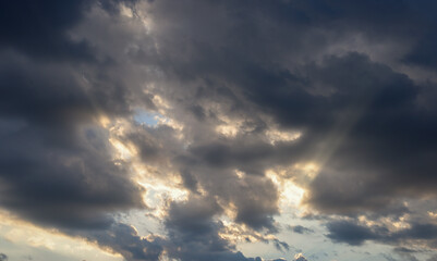 Sunbeams break through dark, stormy clouds, creating a dramatic and dynamic picture of the sky. The image is ideal for illustrating concepts related to natural phenomena, weather changes, hope, and re