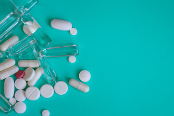 A composition of medical preparations—ampoules, tablets, and capsules—is placed on a turquoise...