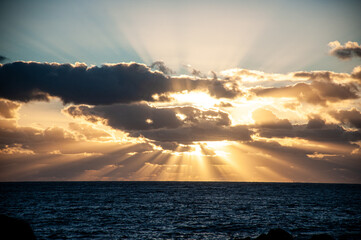 Dramatic sunset over the ocean with golden sun rays breaking through dark clouds