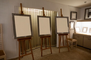 Three empty wooden easels standing in a bright art gallery hall, prepared for upcoming exhibition or painting display, symbolizing creativity, art process, and preparation