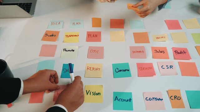 Colorful sticky notes scattered on a table as team members engage in a lively brainstorming session, working together to develop marketing strategies and business plans. SACTR