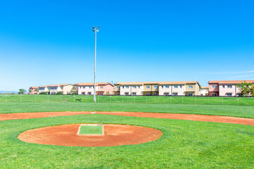 Obraz premium A baseball field with a wide garden surrounding it, offering a view of nearby houses in the distance. The lush green field contrasts with the neighborhood, creating a peaceful, suburban atmosphere.