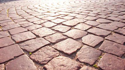 Textured cobblestone pavement with warm sunlight illuminating the surface, showcasing the intricate patterns and natural imperfections of the stones in a serene outdoor setting