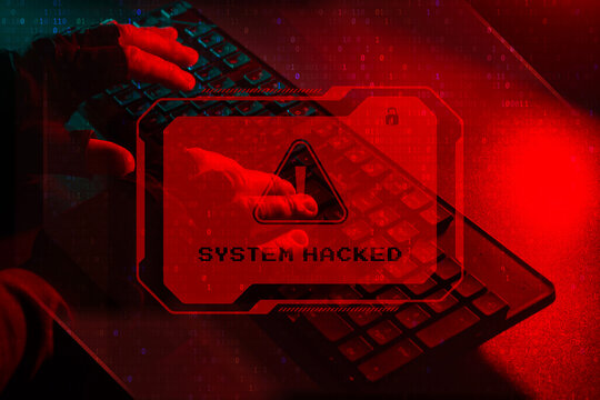 Cyber Attack system hacked concept. Hacker hands typing on a keyboard with a glowing red warning sign System HACKED. - Powered by Adobe