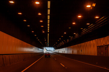 Car driving through a modern road tunnel towards the light at the exit, symbolizing journey and...