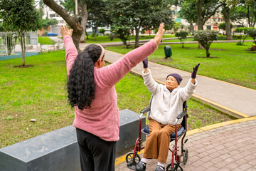Nurse assisting elderly woman in wheelchair doing physical exercises in park