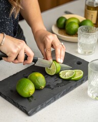 Preparing cocktails woman’s hands cutting limes on a slate cutting board in a home bar setting