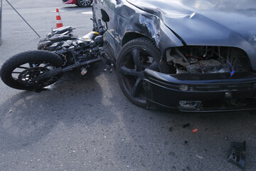 A road accident,a motorcycle lying next to a damaged car with a broken headlight,a warning sign. © Yurginn
