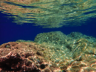 Dark blue ocean surface seen from underwater. Abstract waves underwater and rays of sunlight shining through, Sun light rays undersea deep, Underwater background with sea bottom, Mediterranean sea.