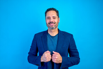 Portrait of a smiling latin American businessman holding his jacket lapels, exuding confidence against a vibrant blue backdrop