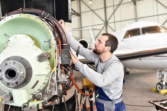 Aircraft mechanic repairs an aircraft engine in an airport hangar