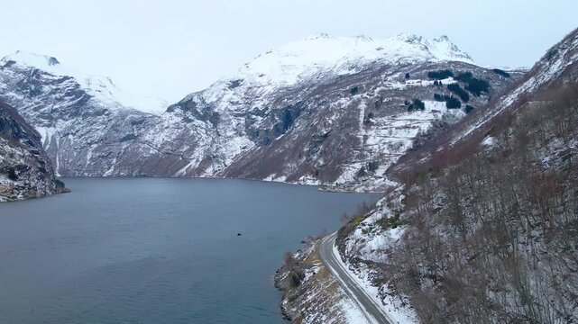 Drone footage capturing the winter scenery of Geirangerfjord, a UNESCO World Heritage site in Norway. The majestic fjord is surrounded by snow covered mountains, showcasing the serene and dramatic bea