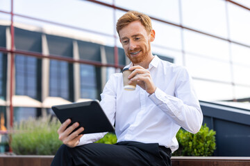 Businessman in white shirt browsing web pages with tablet while drinking coffee on bench outdoor