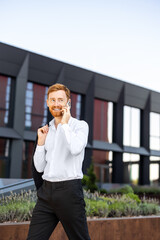 Ginger bearded man walking outdoors in business district speaking on mobile phone