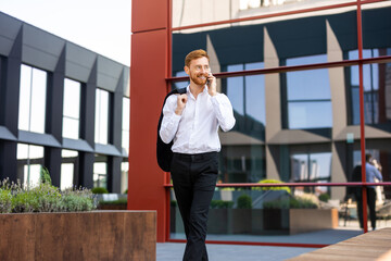 Ginger-haired man in smart outfit holding jacket and having phone conversation