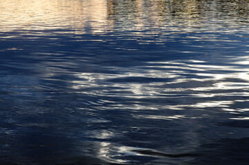Water in a cold river with dark clouds reflected in the water, some sunshine