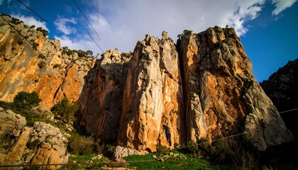 A person slacklines between towering, colorful rock formations in a scenic canyon under a partly cloudy sky.