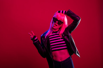 Young woman wearing sunglasses does peace sign and sticks out her tongue in playful studio pose....