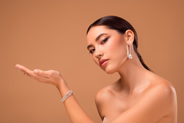 Elegant portrait of a young brunette woman showcasing glamorous jewelry against a beige studio...