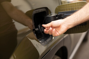 Closeup of man opening EV vehicle inlet port to attach electric cable. Driver opening battery charging port flap of electric car to recharge, making transition to clean energy transportation
