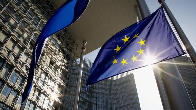 wideangle view of European Union flags waving side by side in front of the European Commission headquarters in Brussels illuminated by sunbeam