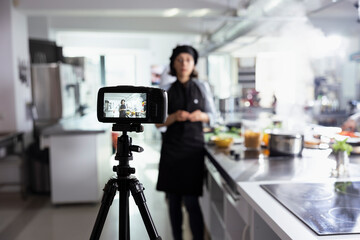 Female chef filming a culinary master class for guiding apprentices through essential cooking skills and techniques. Remote course held in a kitchen, making gourmet training accessible on internet.