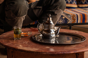 Traditional Moroccan tea served in a silver teapot with a glass of mint tea and nuts on a wooden table inside a cozy setting