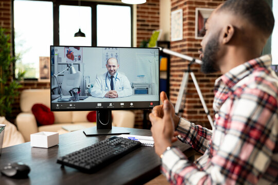 African american self employed man sits at home office desk, having virtual meeting with white male physician on desktop pc. Medical video call focuses on health advice and potential treatment options