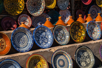 Colorful Moroccan ceramic plates with intricate geometric patterns displayed alongside terracotta tagine pots at a traditional market stall