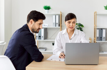 Two cheerful smiling company employees at work in office. Coworkers sitting at the desk on meeting...