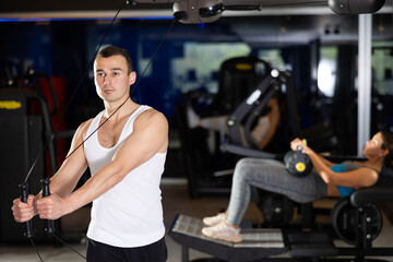 Fototapeta premium Man doing task on loop simulator. He pulls handle with effort. Workout in fitness center, classes to strengthen muscles and create relief. Concept of active and sporty lifestyle