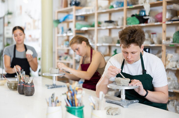 Young man in apron modeling clay pottery in workshop