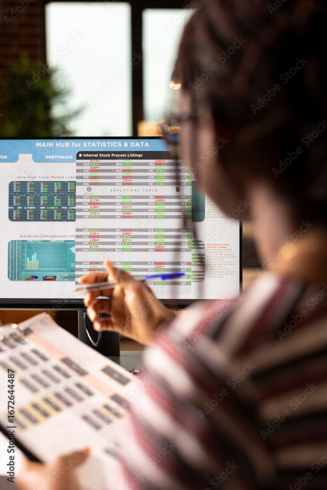 Poster black female freelancer studies analytics on screen while comparing figures from printed documents a