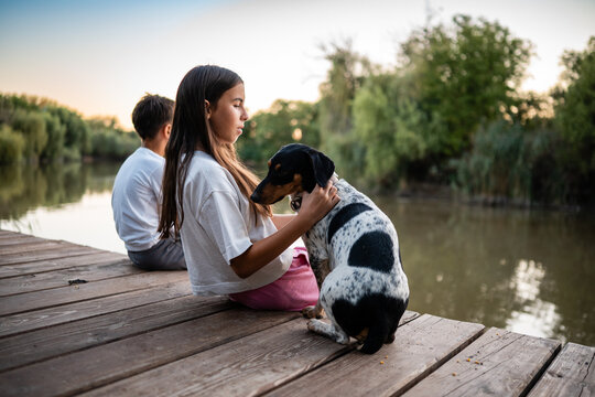 Girl hugging dog on pier with brother at sunset - Powered by Adobe