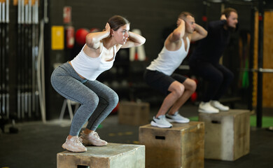 Active young girl squatting on box in sports hall during crossfit workout